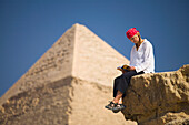 A Female Tourist Reads A Guide Book While Sitting In Front Of The Pyramids Of Giza Near Cairo; Giza Egypt