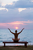 A Woman Tourist Sits On A Bench With Arms Raised At Sunset On The Beach Of A Tropical Island; Koh Lanta Thailand