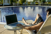 Mann sonnt sich mit einem Laptop an einem Pool, Panama-Stadt, Panama