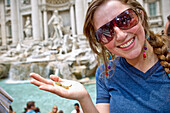 Eine junge Frau hält drei Münzen neben dem Trevi-Brunnen; Rom Italien