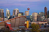 Calgary Skyline mit dem Saddledome Calgary Tower und Gebäuden in der Morgendämmerung mit tiefblauem Himmel und magentafarbenen Wolken; Calgary Alberta Kanada