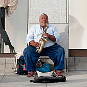 Ein Mann sitzt und spielt sein Saxophon auf dem Bürgersteig; Oslo Norwegen