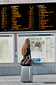 A Woman Stands With Her Luggage Looking At The Map Of Public Transportation Routes; Oslo Norway