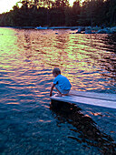 Junger Junge am Ende der Bootsrampe am See bei Sonnenuntergang