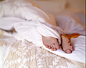Nackte Füße einer Frau ragen aus der Decke auf dem Hotelbett heraus