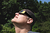 Mittelgroßer Mann mit Sonnenfinsternisbrille bei der Betrachtung einer partiellen Sonnenfinsternis
