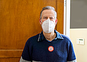 Mann mit Gesichtsschutzmaske und COVID-19-Impfaufkleber auf dem Pullover