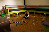 Junger Junge sitzt auf dem Boden eines großen Raumes, umgeben von Plastikspielzeugteilen
