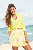 Young brunette woman in a yellow blouse with a knot and a yellow skirt near the sea