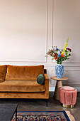 Orange-colored sofa, side table with bouquet of flowers and velvet-covered stool next to it