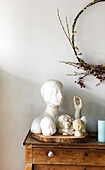 Collection of busts on an old chest of drawers, with a wreath of dried flowers and berries above