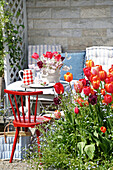 Kleiner gedeckter Tisch im Garten mit rotem Stuhl und Tulpen