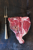 Raw T-bone steak and meat fork