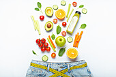 Frisches Obst, Gemüse und Smoothie fallen in Jeans mit gelbem Maßband als Gürtel