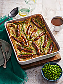 Toad in the hole (fried sausages baked in egg batter, England) with green vegetables