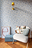 Vintage armchair with cushions in front of a wall with floral wallpaper and yellow lamp