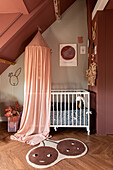 Kinderzimmer mit Dachschräge, Wandgestaltung mit Streifentapete und rostroter Farbe, Gitterbett mit Himmel, Teppich mit Kirschen
