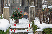 Geschmückter Christbaum mit Wachskerzen auf verschneiter Terrasse und Winterfeuer
