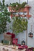 Weihnachtsdeko auf der Terrasse mit Tannenzweigen,  Mistelzweigen, Kerzen an rustikaler Garderobe hängend und Stiefel auf Holztisch