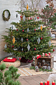 Weihnachtsdeko im Wintergarten, Kerzen, Papieranhänger und bemalte Zapfen vor geschmücktem Christbaum