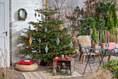 Weihnachtsdeko im Wintergarten, Kerzen und bemalte Zapfen vor geschmücktem Christbaum