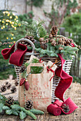 Weihnachtsdeko mit Tannenzweigen, Zapfen, und rotem Band auf Weidenkorb