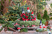 Weihnachtsdekoration, Kranz mit Figuren, Scheinbeere (Gaultheria), Wichtel, Fliegenpilze und Zapfen vor Christbaum auf der Terrasse