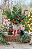 Strauß aus Hagebutten, Seidenkiefernzweigen (Pinus Strobus) in Kaffeetasse und Vogelfigur als Winterdeko auf der Terrasse
