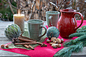 Weihnachtsdeko am Terrassentisch mit Kerze, Kaffeetassen, Tannenzweig, Christbaumkugeln, Zimtstangen und Nüssen