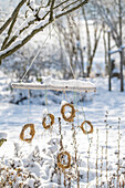 Kleine Minikränze als Windspiel an Baum hängend im verschneiten Garten, Baumschmuck