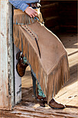 USA, Shell, Wyoming. Cowgirl der Hideout Ranch steht in der Tür mit Cowboystiefeln und Chaps. (PR,MR)
