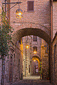 Italien, Umbrien, Assisi. Gasse mit Bögen und Laternen in der Abenddämmerung.