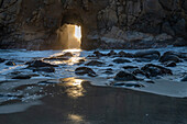 Sun shines through a tunnel in a sea cliff in the Big Sur area.