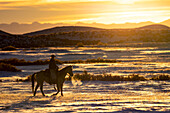 USA, Shell, Wyoming. Hideout Ranch sunset and silhouetted cowboy. (PR,MR)