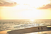Zwei Kinder laufen am Strand bei Sonnenuntergang