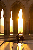 Silhouette of two people walking towards steps and archways with the sun glowing; Casablanca, Morocco