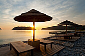 Greece, Crete, Sunshade and Sun Lounger on Beach Opposite Spinalonga Island at Dawn; Spinalonga Island