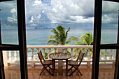 View Through A Doorway Of A Terrace With A Table And Chairs At Petite Anse Hotel. Storm Clouds Gather Over The Ocean; Grenada, Caribbean