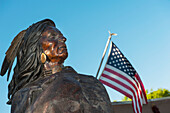 Bronzestatue eines Indianers neben einer amerikanischen Flagge beim Friday Night Canyon Road Gallery Walk in Santa Fe, New Mexico, USA