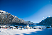 Schneebedecktes Dorf mit Bergen und malerischer Kirche in einem Tal unterhalb der Skipisten in Waidring, Österreichische Alpen, Österreich