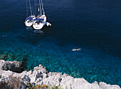 Man Snorkelling Past Two Yachts Moored In Small Bay On The Island Of Bisevo Off Vis, Croatia.