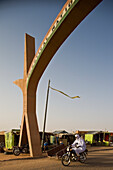 Niger, Sahara Desert, Agadez Region, Veiled Tuareg riding bike crossing city main gate; Agadez