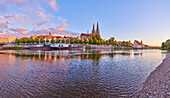 Outlook over the Danube River with the old, 12th Century Stone Bridge in the distance and the Gothic St Peter's Cathedral from the Marc?-Aurel-shore in the Old Town of Regensburg at sunset; Regensburg, Bavaria, Germany