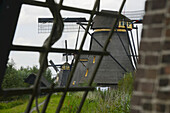 Blick auf eine Reihe traditioneller Windmühlen durch das Gerüst eines Windmühlenflügels; Kinderdijk, Südholland, Niederlande