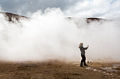 A woman photographs among the steaming mud pots geothermal area near Lake Myvatn.; Iceland
