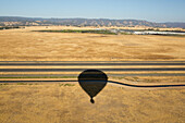 The shadow of a hot air balloon over agricultural fields, irrigation canals, and an interstate.; Winters, California