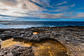 Rock formations and sunlit tidal pools along the coastal shore at Pointe des Chateaux on Grande-Terre with a dramatic cloudy sky; Guadeloupe, French West Indies
