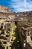 View through the underground tunnels and subterranean floor of the interior of the iconic Colosseum with a blue sky and groups of tourists sightseeing; Rome, Lazio, Italy