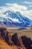 Snow covered Denali with rocky cliffs and colorful foliage on the tundra in  Denali National Park; Alaska, United States of America