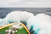 The bow of a ship crashes into oncoming waves.